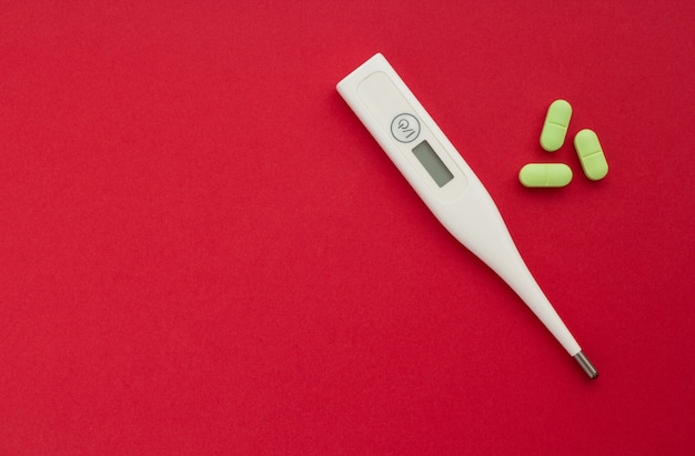 Elektronischer Thermometer mit Tabletten auf einem roten Hintergrund, Konzept der Gesundheit