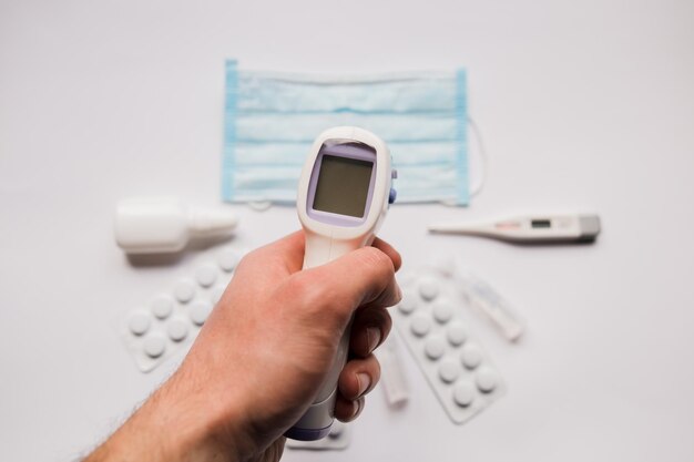 Elektronisches Thermometer in der Hand mit medizinischer Maske