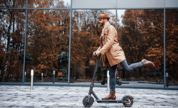 Elektroroller fahren Junges männliches Model in modischer Kleidung ist tagsüber draußen in der Stadt