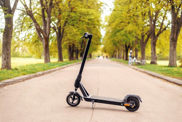 Elektroroller im Park. Kreuzfahrt zwischen den orange-grünen Bäumen auf einer Straße. Moderner Öko-Transport. Sorge um die Umwelt.