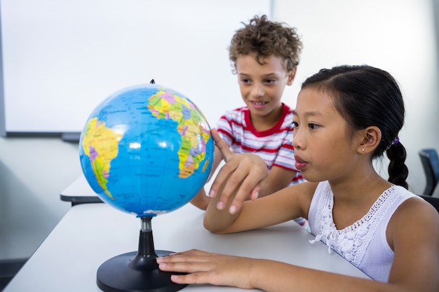 Elementar menino e menina olhando glob na sala de aula