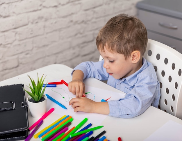 Elementarer Junge, der zu Hause niedliche fröhliche Kinderzeichnung lernt