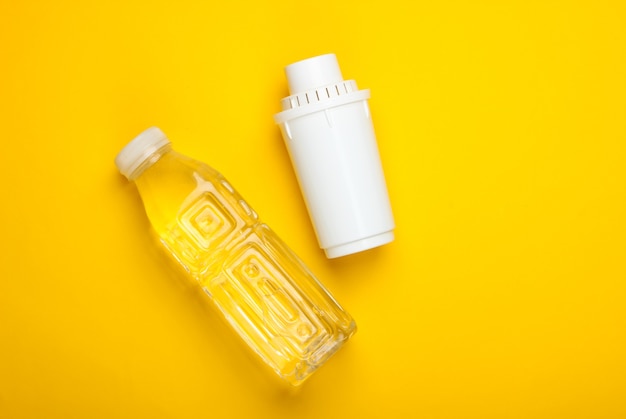 Elemento filtrante de purificador de agua y botella de agua pura sobre fondo amarillo. Vista superior