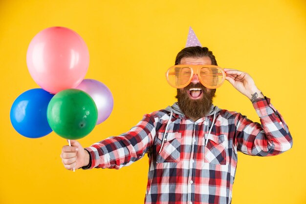 Foto elementos de fiesta jóvenes y despreocupados y objetos de vacaciones diversión multicolor mejor fiesta para jubilación hombre alegre con barba y bigote hipster sonriendo con globo celebrando fiesta feliz