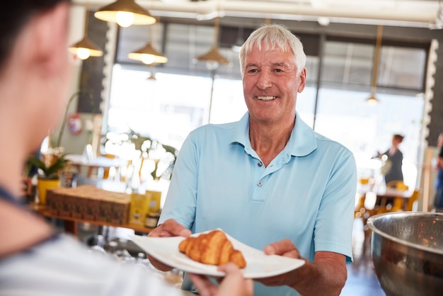 Eles servem frescos eles servem melhor Foto de um homem sênior feliz sendo servido com um croissant em um café
