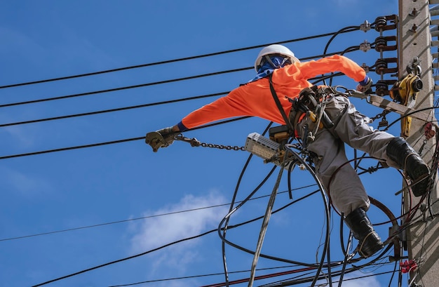 Eletricista com ferramentas de trabalho está instalando linhas de cabos e sistema elétrico no poste de energia elétrica