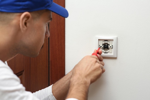 Eletricista profissional com chave de fenda reparando o interruptor de luz em ambientes fechados