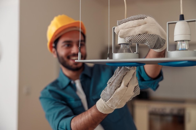 Foto eletricista profissional de uniforme está instalando as lâmpadas no candelabro em casa