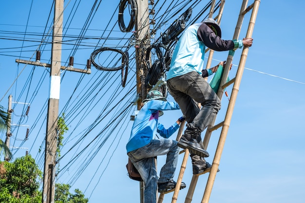 Foto eletricista subindo a escada de bambu para reparar fios elétricos.