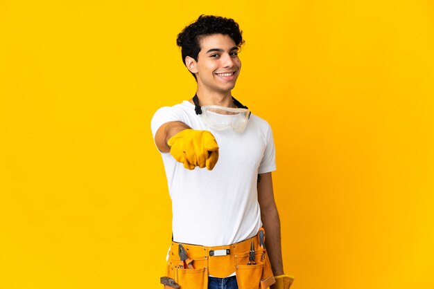 Eletricista venezuelano isolado em um fundo amarelo apontando para a frente com uma expressão feliz