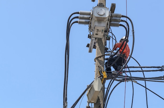 Eletricistas estão escalando postes elétricos para instalar e consertar linhas de transmissão.