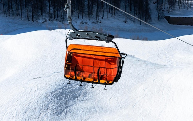 Elevador de cadeira de esqui laranja brilhante vazio no inverno das montanhas contra a neve Esqui alpino e snowboard