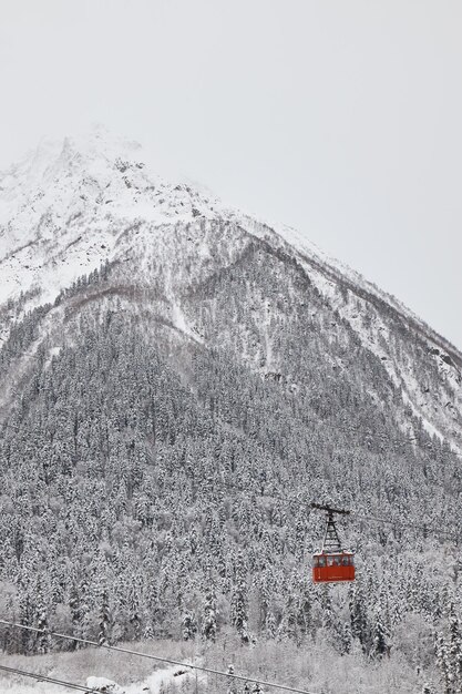 Elevador de pêndulo no teleférico das montanhas, cabine vermelha, neve de inverno nas encostas e ela na floresta