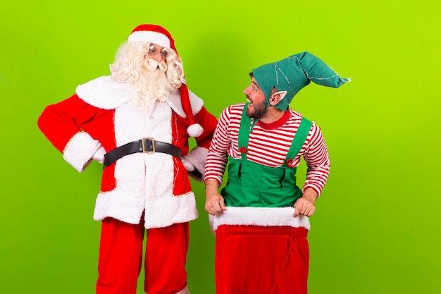 Foto elfo y papá noel juntos y felices sobre fondo verde sonriendo a la cámara