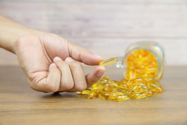 Elija a mano una cápsula de aceite de hígado de bacalao de una pila de aceite de hígado de bacalao o suplemento dietético de aceite de pescado para conceptos de cuidado de la salud.