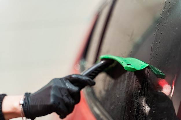 Eliminación de agua residual del vidrio con un raspador de goma después de lavar el automóvil. Car Wash. Complejo de autoservicio. Lavado de autos a alta presión.