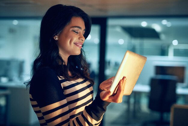 Ella aprovecha cada minuto del día Foto de una joven empresaria que trabaja hasta tarde en una tableta digital en una oficina