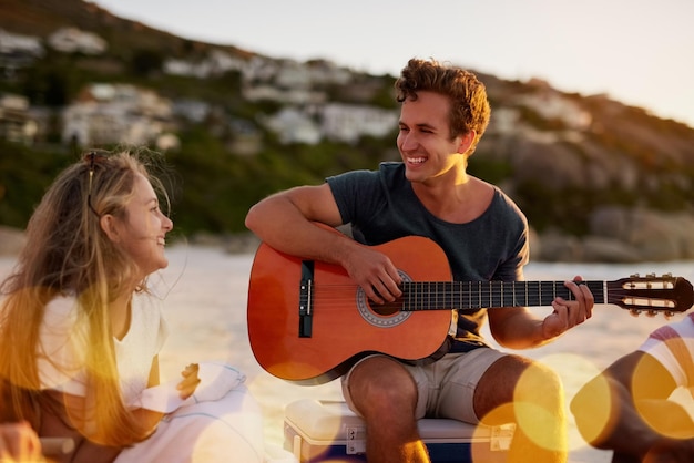 Ella es mi inspiración Foto de un hombre tocando la guitarra mientras está sentado en la playa con su novia