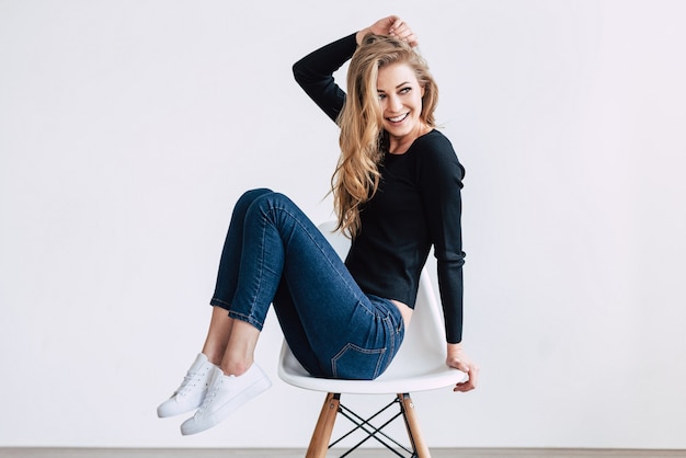 Ella es simplemente hermosa. Hermosa mujer joven posando y mirando a otro lado con una sonrisa mientras está sentado en una silla contra el fondo blanco.