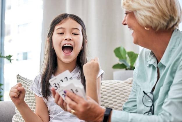 Ella está superando sus horarios. Foto de una niña y su abuela jugando a las cartas en casa.