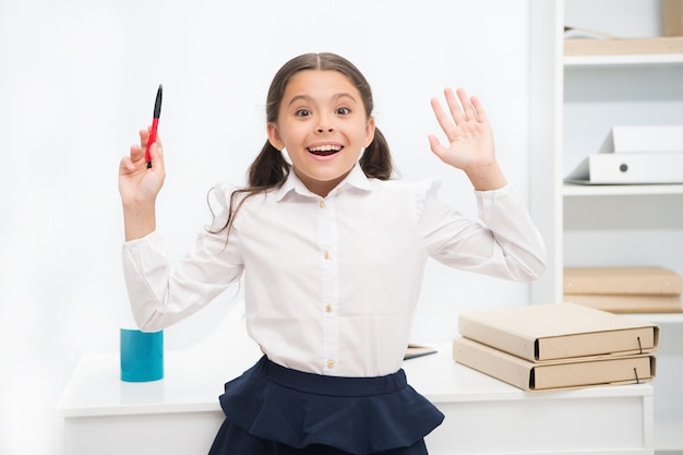 Ella sabe la respuesta correcta. La muchacha del niño viste la expresión de la cara emocionada de pie uniforme escolar. Niño inteligente colegiala parece emocionado fondo interior blanco. Chica recuerda la respuesta correcta. Listo para responder.