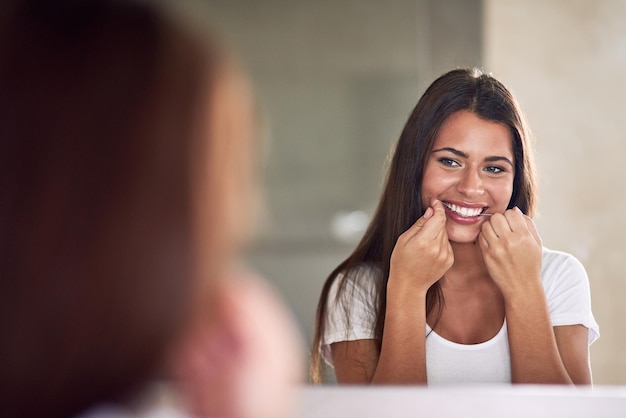 Ella siempre escucha a su dentista fotografía de una mujer hermosa que se pasa hilo dental mientras se mira en el espejo