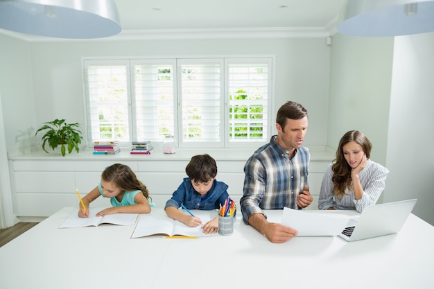 Eltern arbeiten mit Laptop und Kinder, die im Wohnzimmer studieren