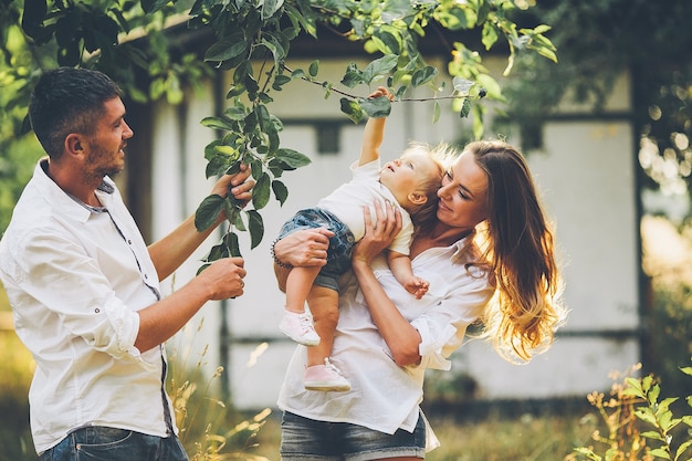 Eltern mit Baby genießen Picknick auf einem Bauernhof mit Apfel- und Kirschbäumen.