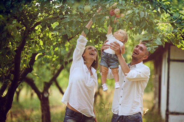 Eltern mit Baby genießen Picknick auf einem Bauernhof mit Apfel- und Kirschbäumen.