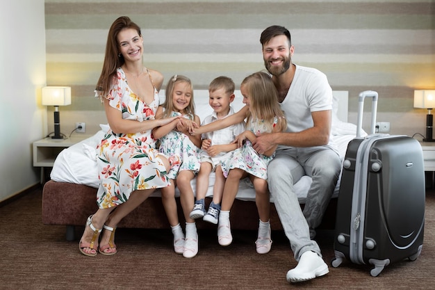 Eltern mit Kindern sitzen auf dem Bett im Hotel und lachen Reisen mit Kindern