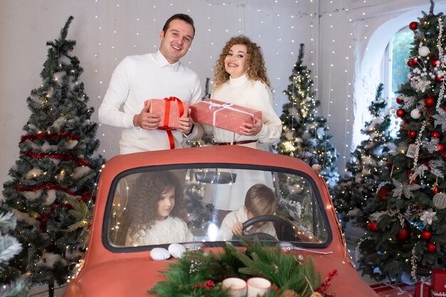 Eltern und ihre Kinder haben Spaß im roten Auto in der Nähe von Weihnachtsbäumen.