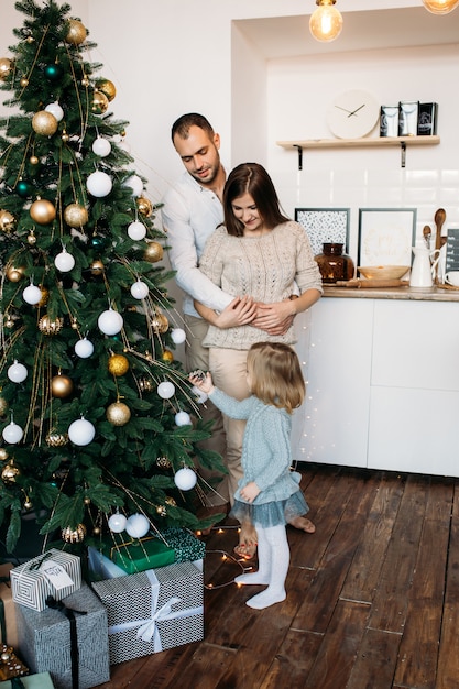 Eltern und kleine Tochter, die zu Hause Weihnachtsbaum verzieren. Frohe Weihnachten und ein glückliches Neues Jahr!