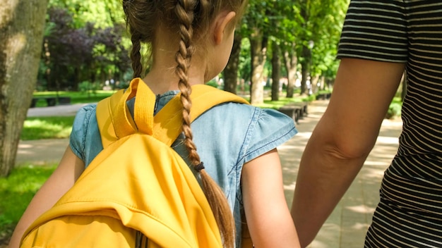 Eltern und Schüler der Grundschule gehen Hand in Hand. Mutter und Tochter gehen durch die Parkgasse