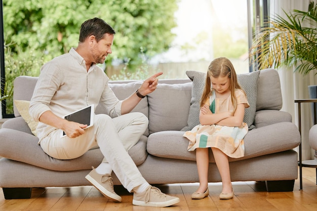 Elternkind und Tablet mit Disziplin auf einem Sofa im Wohnzimmer für ungezogenes Verhalten zu Hause Verärgert wütender und junger strenger Vater spricht mit traurigem Mädchen Kind auf der Couch in der Lounge in einem modernen Haus