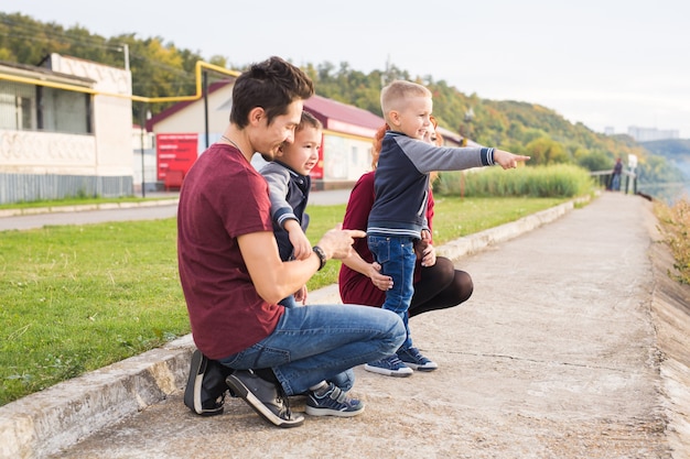 Elternschaft, Kindheit und Familienkonzept - Eltern und zwei männliche Kinder, die im Park spazieren und etwas anschauen.