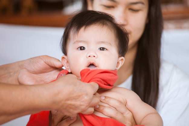 Elternteil kleidet ihr asiatisches Baby mit Sorgfalt und Liebe