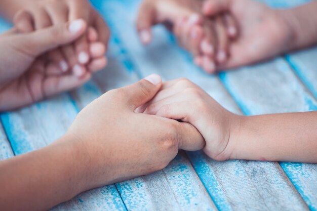 Elternteil- und Kinderhändchenhalten und zusammen beten auf blauem Holztisch