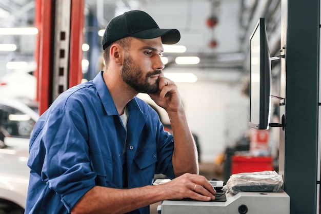 Em boné preto Usando computador Mecânico de automóveis trabalhando na garagem Serviço de reparação
