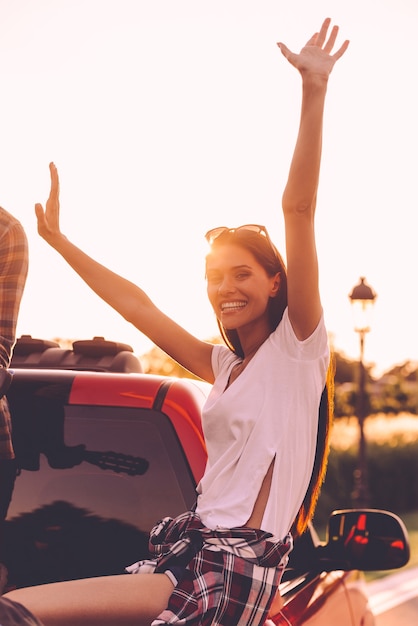 Em busca de aventuras. Mulher jovem e bonita de braços erguidos e sorrindo enquanto aproveita a viagem em uma caminhonete.