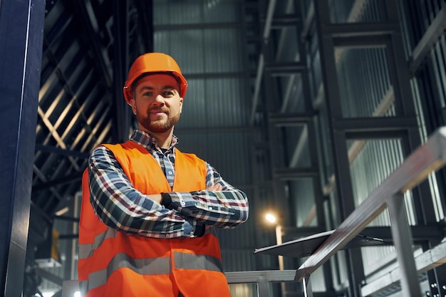 Em capacete de cor laranja Trabalhador da construção civil de uniforme está na fábrica