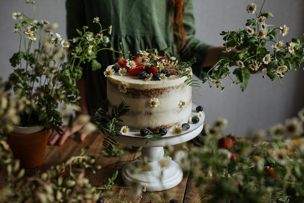 Em cima da mesa há um bolo decorado com frutas e flores