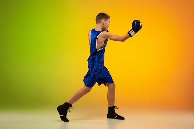 Em movimento. Boxer profissional adolescente treinando em ação, movimento isolado em fundo gradiente em luz de néon. Chutando, boxe. Conceito de esporte, movimento, energia e estilo de vida dinâmico e saudável.