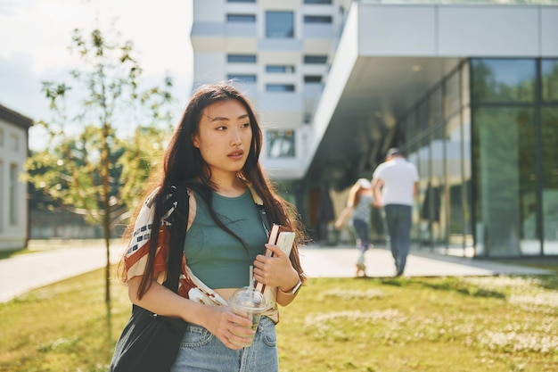 Em pé contra o edifício moderno a jovem asiática está ao ar livre durante o dia