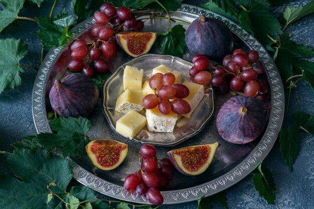 em prato de prata uvas vermelhas, figos e queijo