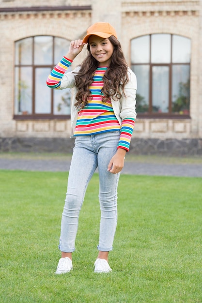 Em seu próprio estilo, felicidade infantil, garota feliz, com cabelos longos e encaracolados, criança bonita sorrindo ao ar livre