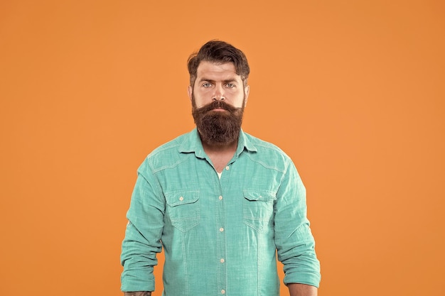 Em seu próprio estilo Homem sério fundo laranja Homem barbudo em estilo jeans casual Loja de roupas masculinas Homem caucasiano usa bigode e barba Olhar hipster de homem brutal Barbearia