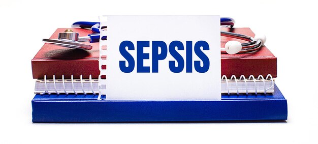 Em um bloco de notas de fundo claro, um estetoscópio e um cartão branco com o texto SEPSIS. Conceito médico