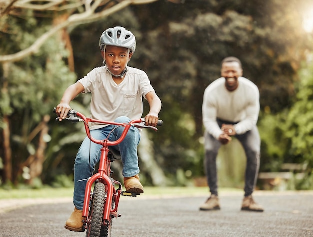 Em um cavalo de aço eu monto. Foto de um menino adorável aprendendo a andar de bicicleta com seu pai ao ar livre.