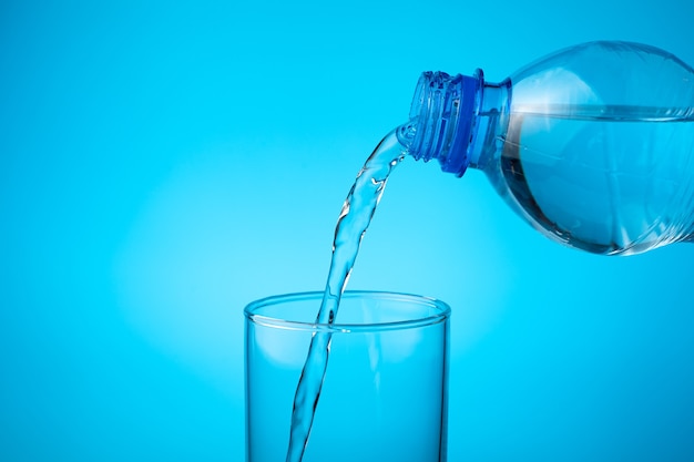 Em um copo vazio, despeje água doce sobre um fundo azul.