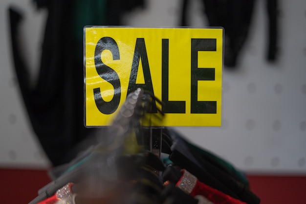 Foto em um fundo amarelo em letras pretas escrevia a palavra venda. vitrine de roupas femininas